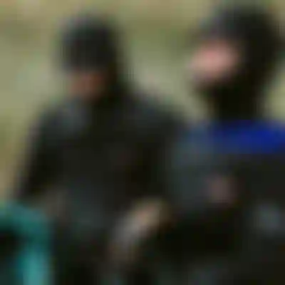 Two people wearing ION black hooded wetsuits and gloves preparing kitesurfing equipment outdoors in cold weather conditions.