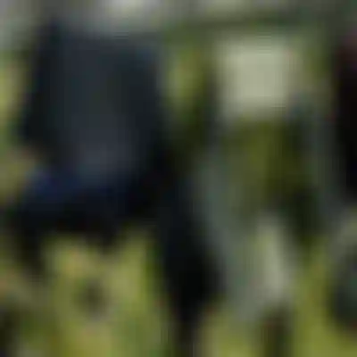 Three wetsuits hanging on an outdoor clothesline to dry, including a black ION suit and a green patterned suit inside out, with a green background.