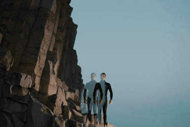 Man and woman in wetsuits standing on a cliff near the sea