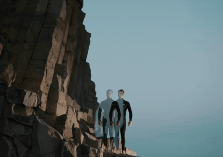 Man and woman in wetsuits standing on a cliff near the sea