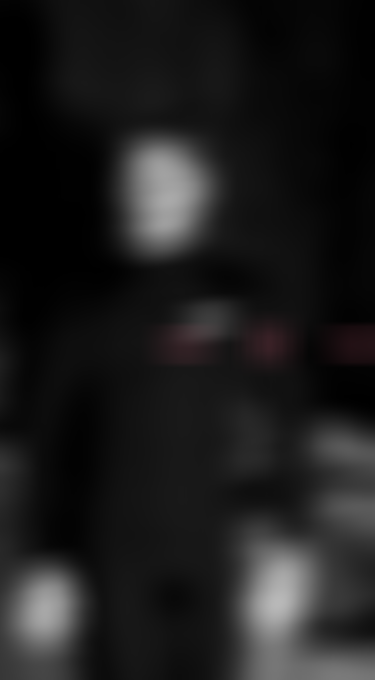 Blurred black and white image of a person in a dark wetsuit, standing against a shadowy background with pink accents.