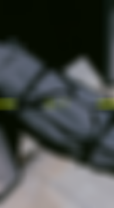 A gray duffel bag with black straps lies partially in shadow on a tiled floor. The bag features a small printed globe and palm tree icon.