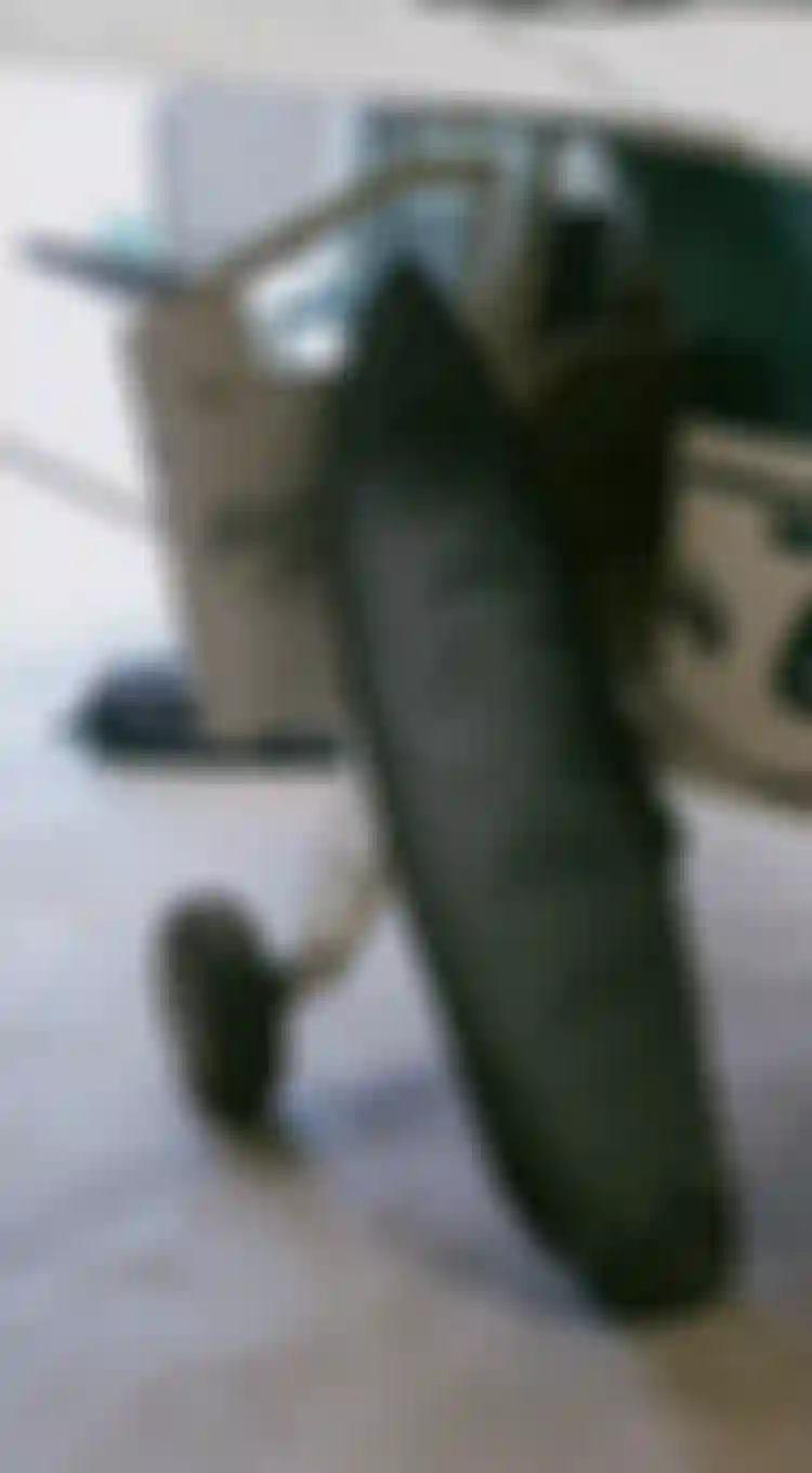 Surf boardbag in a gray cover leans against a small aircraft's open door in a hangar. The plane's fuselage has green and white markings.