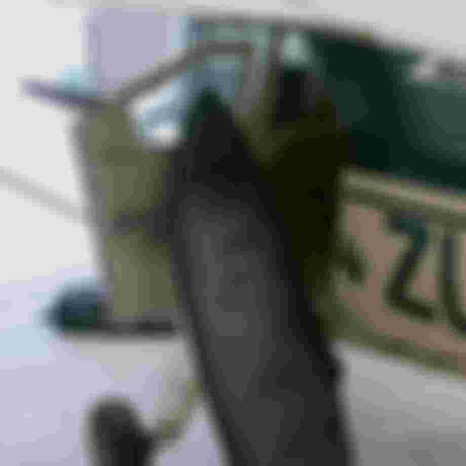 Surf boardbag in a gray cover leans against a small aircraft's open door in a hangar. The plane's fuselage has green and white markings.