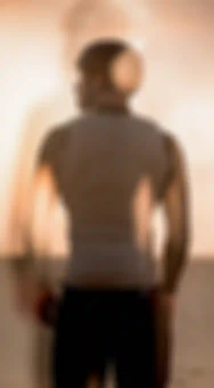 A person wearing a impact vest and helmet looks at a sunset on a beach. The image has a warm, dreamy double exposure effect.