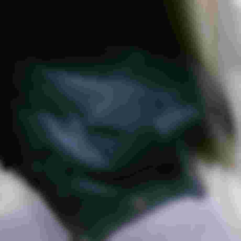 Blurred image of a dark backpack with white text partially visible, placed inside a compartment, suggesting movement or travel.