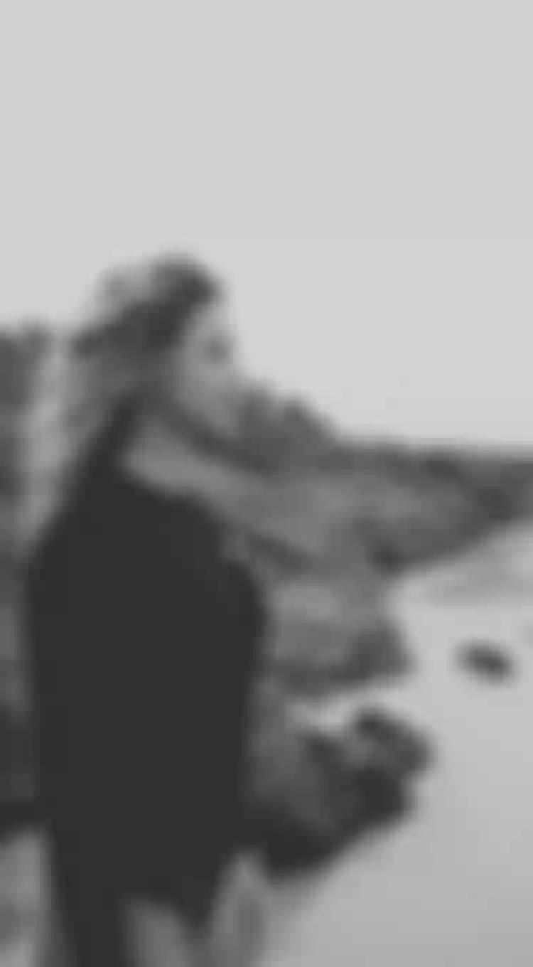 Woman wearing a lycra standing on a beach with rocks in the background
