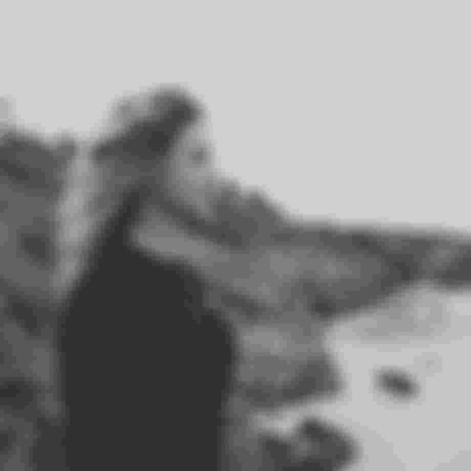 Woman wearing a lycra standing on a beach with rocks in the background