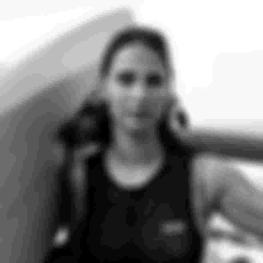Black and white photo of a woman holding a foil board, wearing a wetsuit, with wet hair and a focused expression.