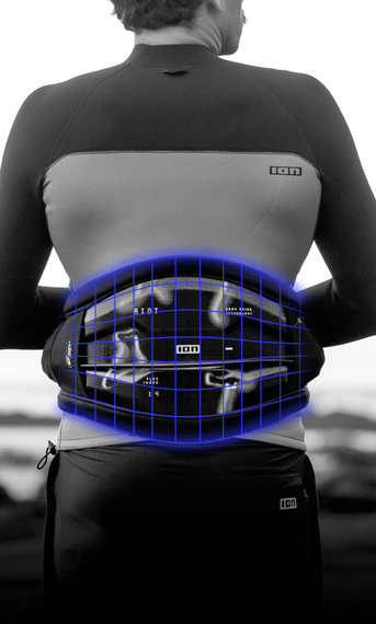 Person wearing a wetsuit and a harness with a glowing grid pattern on the back, standing near the ocean with rocks in the background.