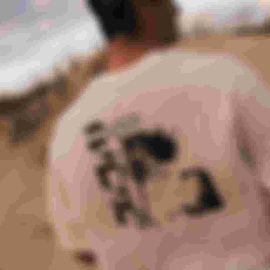 Man wearing a white graphic t-shirt and gray cap, standing outdoors, with "It's about the unexpected" text visible on the shirt.
