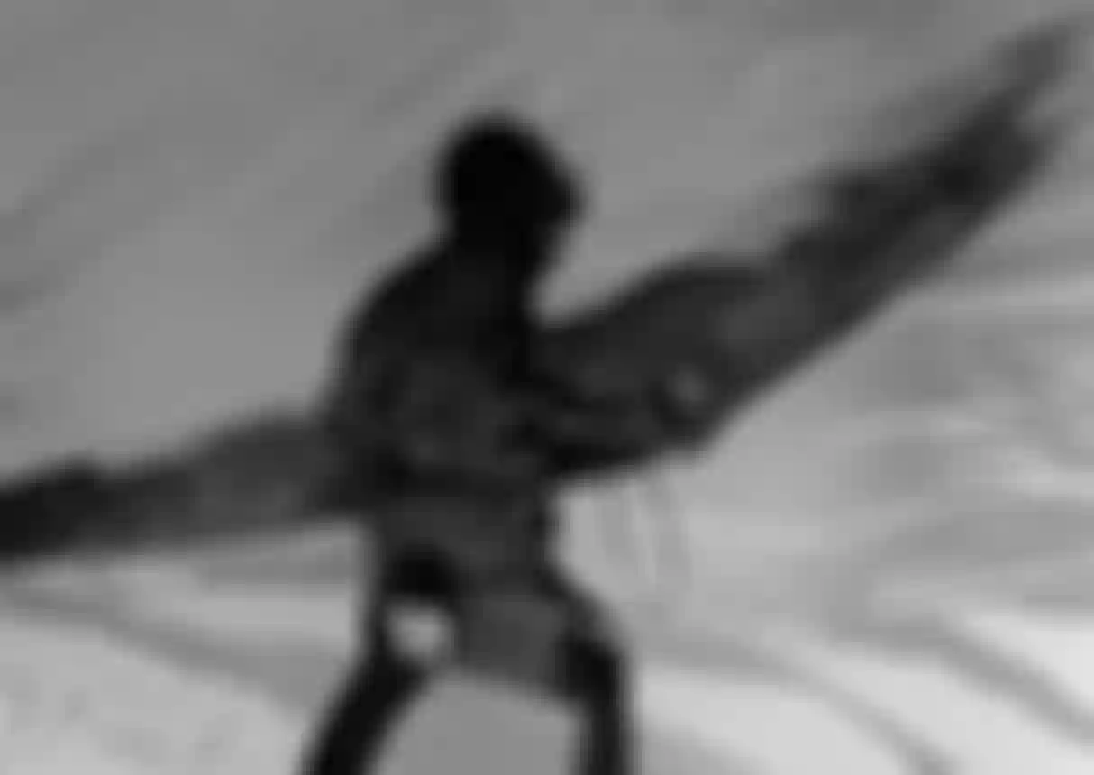A black and white image of a person wearing a helmet, holding a wing, with abstract water-like patterns overlaying the background.