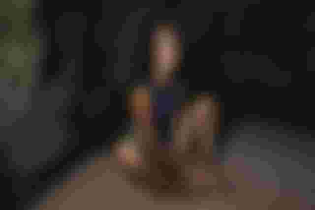 Person sitting on sandy ground, leaning against a rocky wall. The lighting casts shadows, creating a dramatic effect.