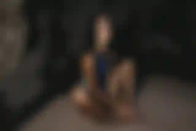 Person sitting on sandy ground, leaning against a rocky wall. The lighting casts shadows, creating a dramatic effect.