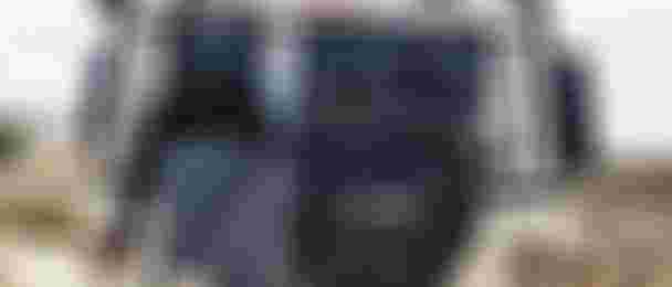 Rear view of an off-road vehicle with kite gear, including a harness, hat, and jacket, attached to the back. Desert landscape in the background.