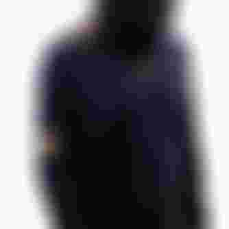 Person in a black helmet and biking gear looks down, featuring gold accents and logos on the shirt and sleeves, against a light background.