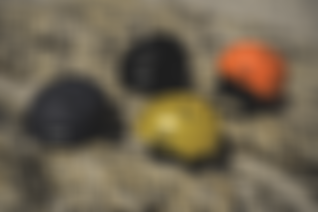 Four colored helmets laying on a rocky, sandy surface