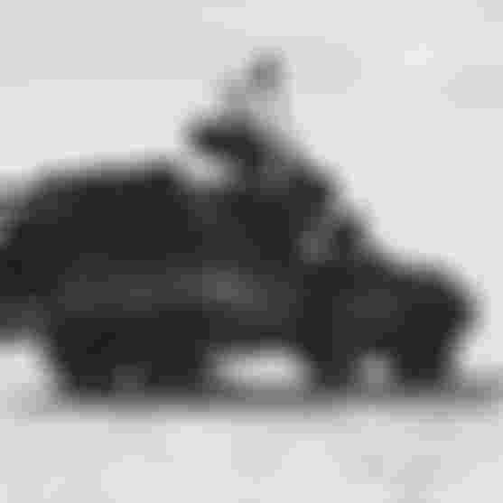 Black-and-white photo of two people loading duffel bags onto a pickup truck's roof rack on a sandy beach with open tailgate.