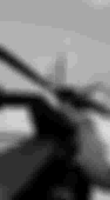 Person securing a surfboard on a vehicle roof rack with straps, preparing for transport. Black and white image.