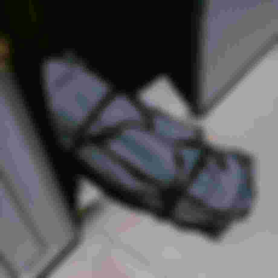 A large, grey, wheeled bag is halfway out of a container opening onto a sunlit concrete surface.