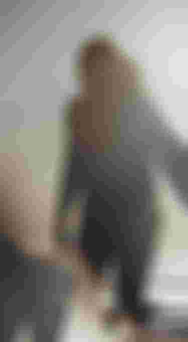 Silhouetted person with kite surfboard walking on a sunlit beach, with a bright sun flare in the background.