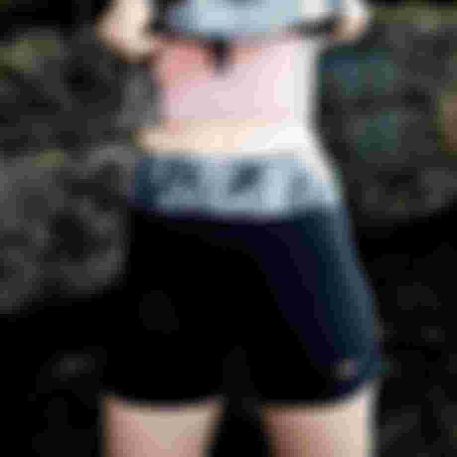 A person wearing a patterned athletic top and black shorts stands in front of a rocky background.