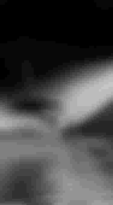 Black and white image of a person wakeboarding, creating a large spray on a calm lake, with motion blur capturing speed and action.