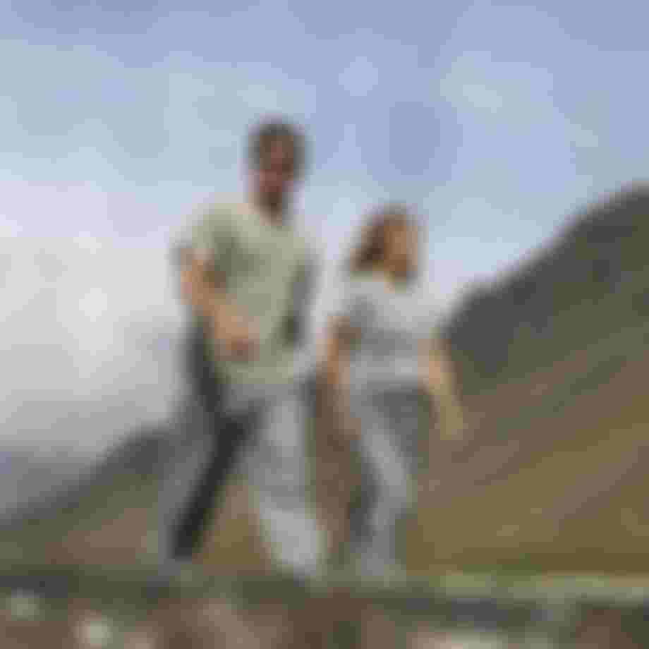 Two people walking next to each other wearing grey cotton pants with green mountains in the back
