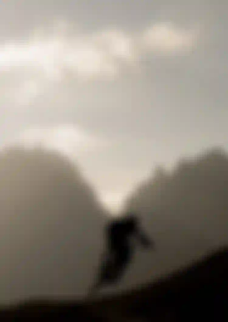 Silhouette of a mountain biker airborne against a backdrop of misty mountains and a bright sky.