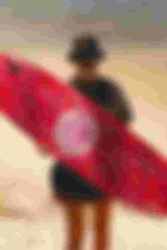 Woman holding a pink kiteboard standing on a beach