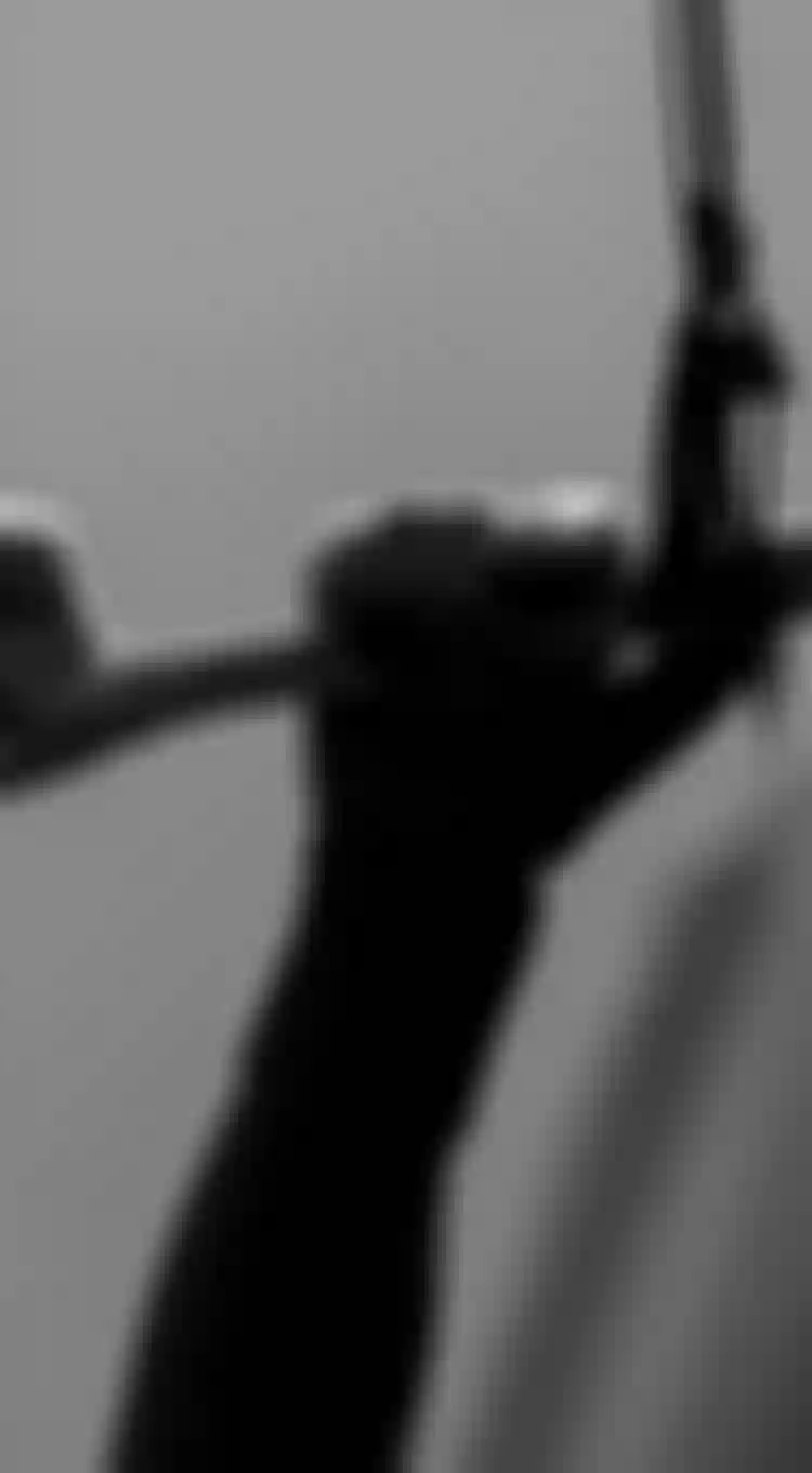 Black and white close-up of a gloved hand gripping a kite bar with lines and connectors visible against a grey sky.