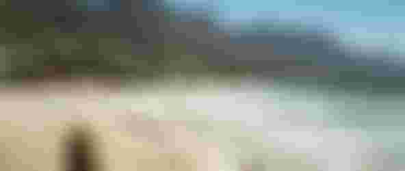 Analog picture of a sandy beach and waves breaking in green-blue water with smooth rocks in the foreground