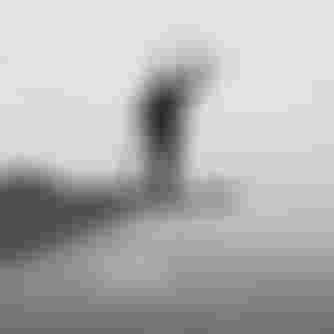 Black and white image of a man carrying a kiteboard and kite in the air