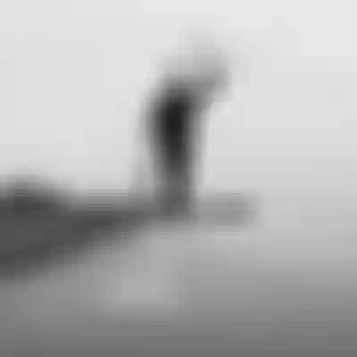 Black and white image of a man carrying a kiteboard and kite in the air