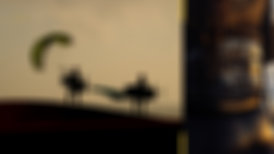 Silhouettes of two surfers with foil boards and a parawing at dusk. Close-up on wetsuit with water droplets on the right.