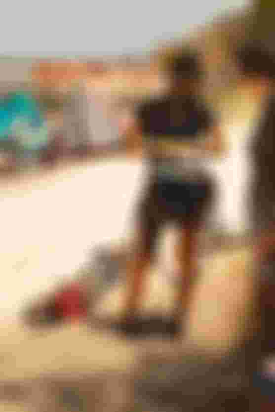 Woman in a black t-shirt with white ION logo holding a kite harness standing on a beach with kites in the background