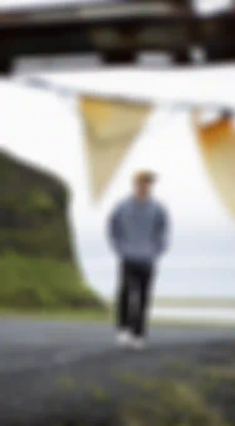 Man walking on a black beach with green hills in the background