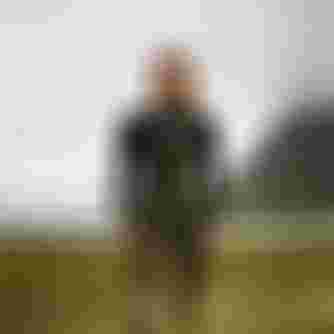 Woman wearing a black wetsuit standing in a field with low hanging clouds in the background