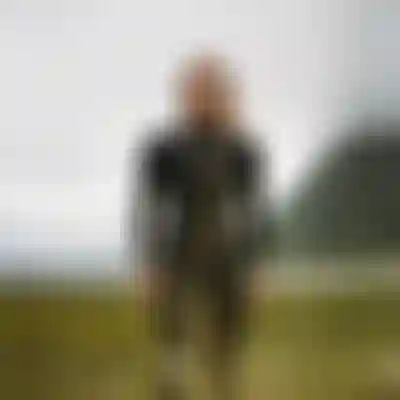 Woman wearing a black wetsuit standing in a field with low hanging clouds in the background