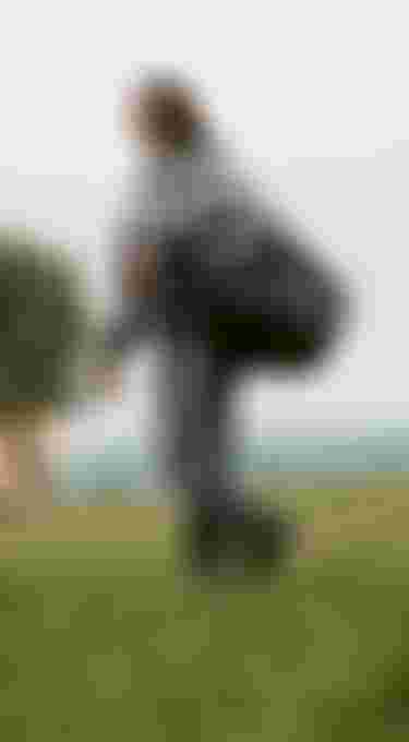 Woman in grey denim jacket and pants carrying a big duffle bag while walking on grass