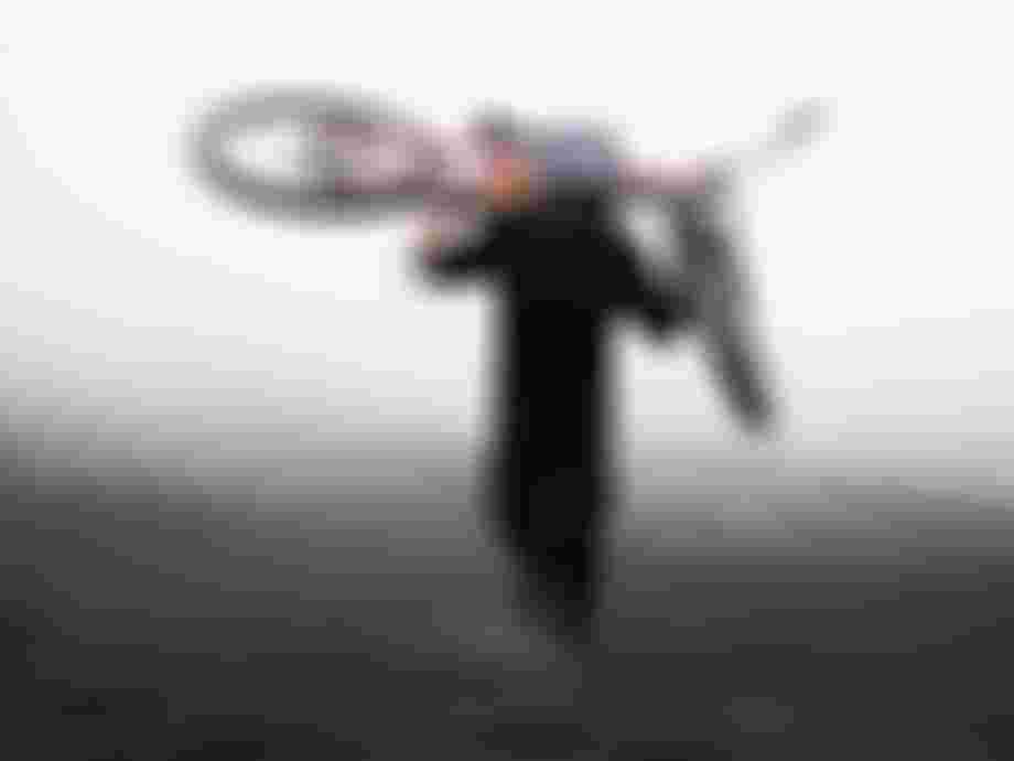 Person in black gear carrying a pink mountain bike on their shoulder, walking on a misty, rugged terrain.