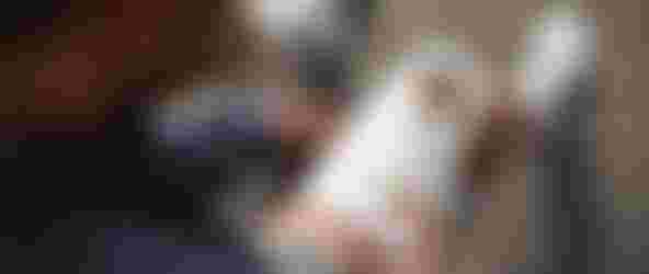 A person applying a white adhesive wrap to their knee while sitting on a carpet, wearing a blue shirt and white socks.