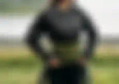 Woman putting on a wetsuit over a black long sleeve rashguard