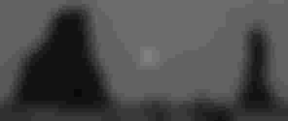 Three people standing on a rocky beach at night in Iceland with the full moon rising in the background