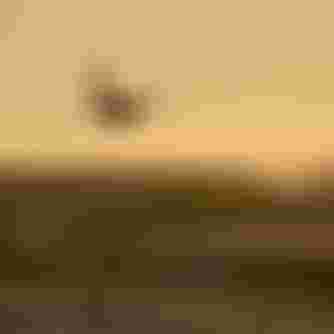 A kiteboarder performs an aerial trick over ocean waves at sunset, silhouetted against a golden sky.