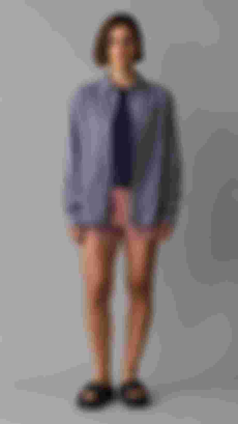 Women standing in front of a grey background wearing pink shorts and a denim blue shirt