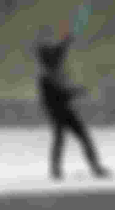 Man wearing a black wetsuit and neoprene jacket with hood on a kiteboard standing on the beach