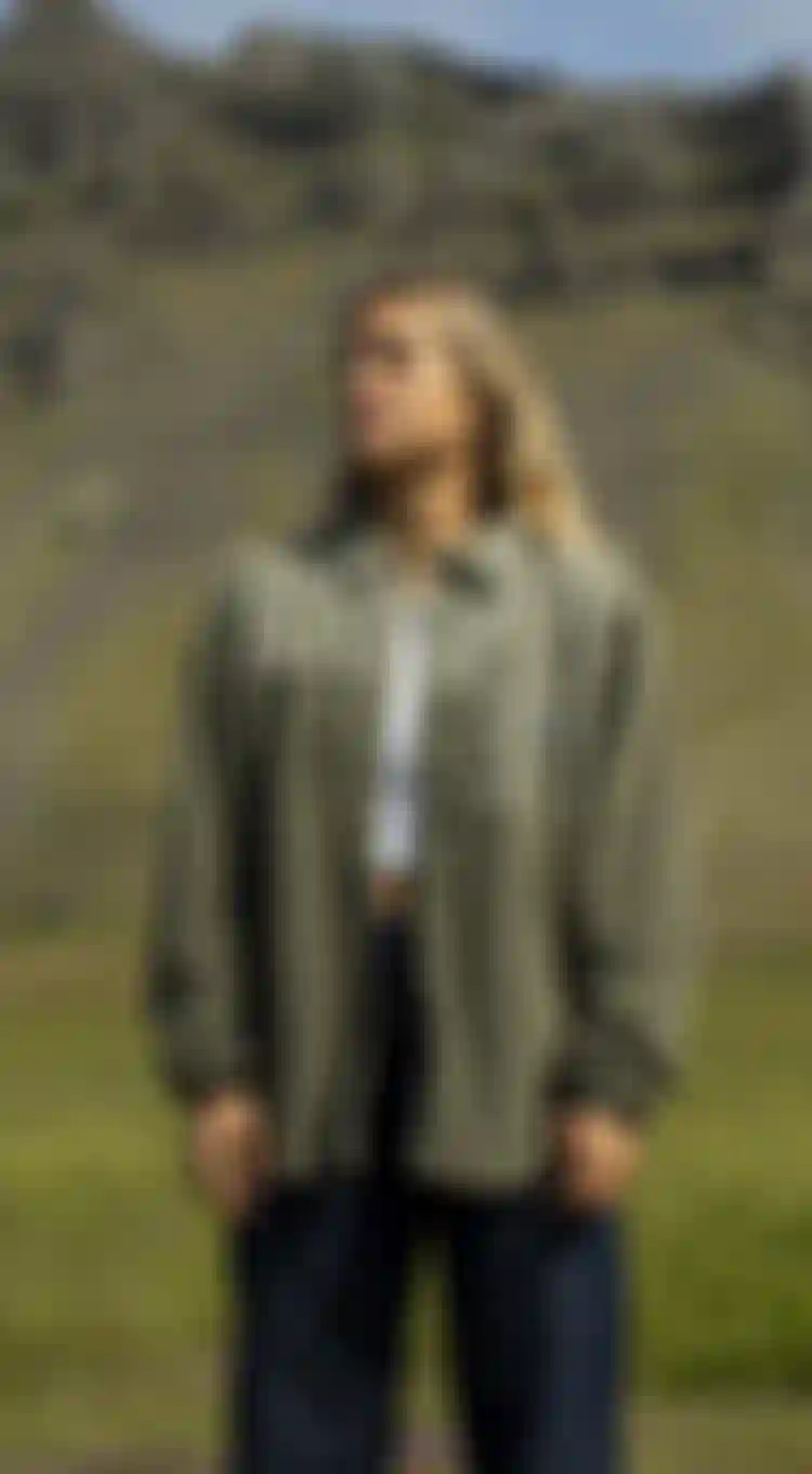 Camille Losserand wearing the IONIC Fleece while standing in front of a green hill in Iceland