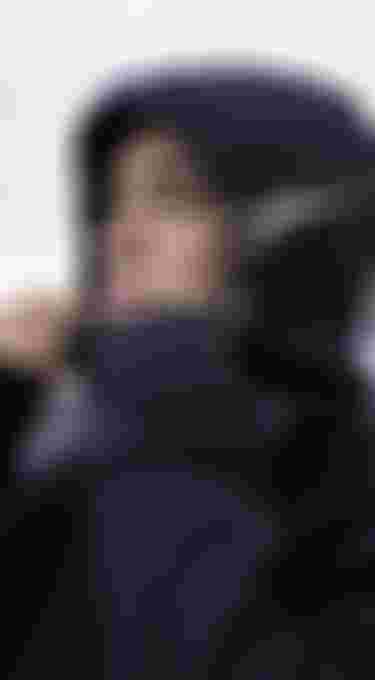 Close up of a woman wearing a black neoprene jacket with hood, blurred beach with black sand in the background