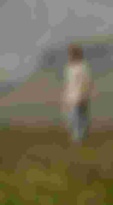 Man standing on grass in front of a mountain landscape